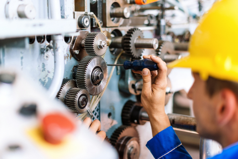 Werker mit Helm schraubt an einer Industriemaschine